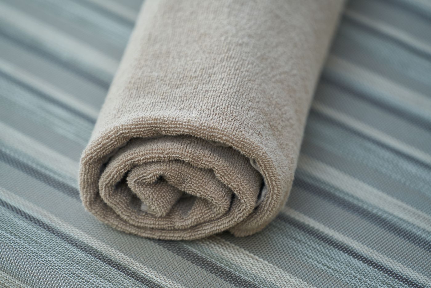 Neatly rolled beige towel on striped linen